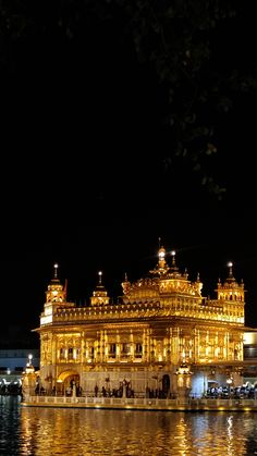 the golden building is lit up at night with lights reflecting in the water below it