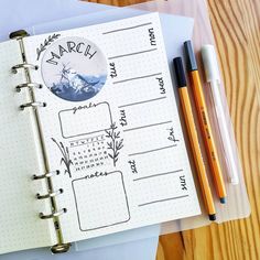 an open planner and pen sitting on top of a wooden table