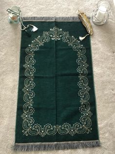 a green table runner with gold trimmings sits on the floor next to some glasses