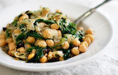 a white bowl filled with beans and spinach on top of a table cloth next to a fork