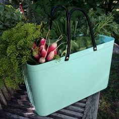 a blue tote bag with radishes and greens in it sitting on a bench