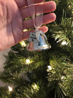 a hand holding a bell ornament in front of a christmas tree