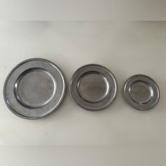 three metal plates sitting next to each other on a white counter top in front of a wall