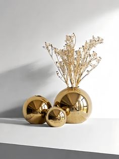 two gold vases with flowers in them on a white surface, next to each other