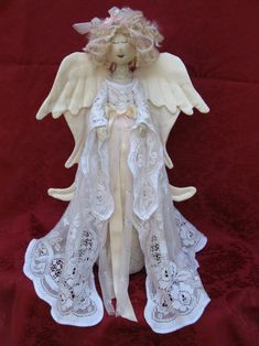 an angel doll is sitting on a red cloth with white lace around it's wings