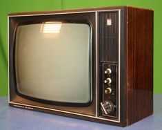 an old fashioned television sitting on top of a blue tableclothed surface in front of a green wall