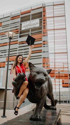 a woman in a red dress is holding up a black book and posing next to a statue of a tiger