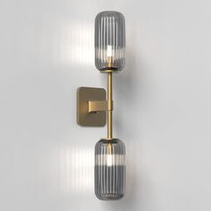 two lights that are next to each other on a white wall, one is gold and the other is clear