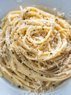 a white plate topped with pasta covered in cheese and black pepper sprinkles