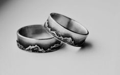 two wedding rings sitting on top of a white table next to each other with mountains in the background