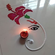 a lit candle sitting on top of a white floor next to a flower design painted on the ground