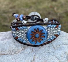 Blue Sun and Brown Leather Wrap Bracelet  The length of the bracelet is the inside circumference when the bracelet is clasped  This Bracelet Features 2mm Round Brown Genuine Leather A glass Blue Sun Bead 20mm Blue and Brown superduo beads (2 hole) beads 8/0 Silver seed beads Moon and Stars Button 17mm The Bracelet width is 1" at the widest point This Bracelet is so comfortable to wear it will really surprise you, and an excellent addition to any outfit! All Bracelets are hand made and are create Superduo Beads, Boho Cuff Bracelet, Beaded Leather Wraps, Boho Cuff, Super Duo, Star Buttons, Bracelet Blue, Blue And Brown, Bead Leather