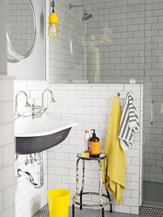 a white tiled bathroom with yellow and black accessories on the shower stall, sink and mirror