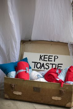 an open suitcase filled with red and blue blankets sitting on the floor next to a sign that reads keep toastie