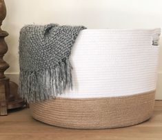 a white and grey basket sitting on top of a wooden floor next to a lamp