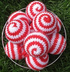 four red and white striped balls in a basket on the grass with green grass behind them