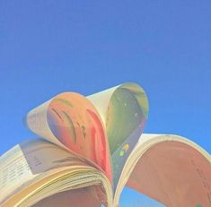 an open book sitting on top of a beach next to the ocean and blue sky