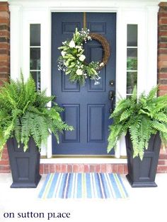 two large planters are on the front porch with blue door and white trimming