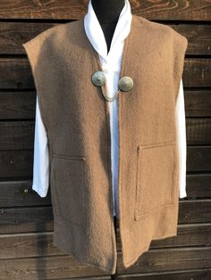 A long folk-style woollen waistcoat in a very nice brown colour, similar to cocoa. The waistcoat is fastened with a single decorative metal buckle at the front, which has a chain on either side of the waistcoat. There are two large pockets at the sides. The waistcoat is long, warm and unlined. A great gift to keep yourself or a loved one warm. Material: wool. Size: no size label, most will fit true to size EU 42, UK 14, XL (X Large). Please also check the measurements at the bottom: MEASUREMENTS Brown Wool Sweater Vest For Workwear, Brown Wool Vest For Workwear, Brown Wool Vest For Work, Brown Buttoned Sweater Vest For Fall, Brown Wool Sweater Vest For Fall, Brown Winter Sweater Vest For Workwear, Wool Sweater Vest With Buttons For Fall, Wool Vest Outerwear For Fall, Brown Buttoned Vest For Winter