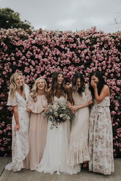 a group of women standing next to each other in front of a flower covered wall