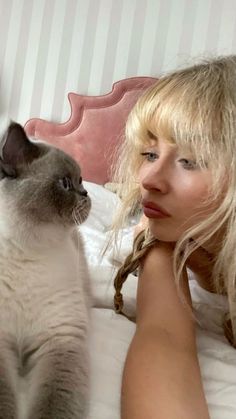 a woman laying on top of a bed next to a gray and white cat with blue eyes