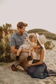 a man, woman and child are sitting on the sand