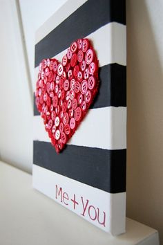 a heart made out of buttons sitting on top of a white shelf next to a black and white striped wall