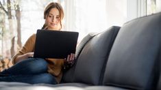 a woman sitting on a couch with a laptop computer in her hand and looking at the screen