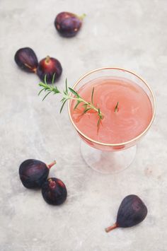 a small glass filled with a pink drink surrounded by figs on a marble surface