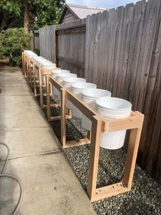 a row of white buckets sitting on top of a wooden stand next to a fence