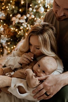 a man and woman holding a baby in front of a christmas tree