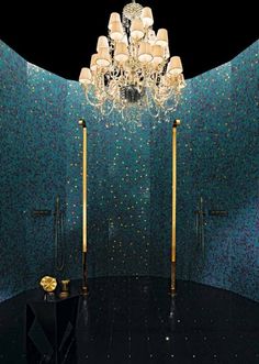 a chandelier hanging from the ceiling in a blue tiled bathroom with gold fixtures