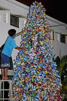 a man standing on a ladder next to a large christmas tree made out of cans