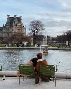 two people sitting on green chairs in front of a water fountain and large stone building