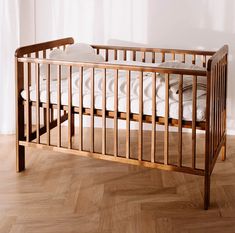 a wooden crib with white sheets and pillows on it's sides, in front of a window