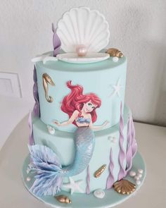 a three tiered cake decorated with an image of a mermaid on the bottom and under it