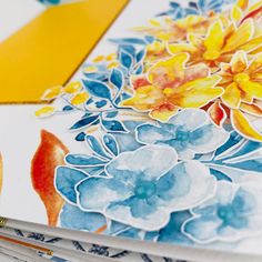 an open book with watercolor flowers and pencils next to it on a table