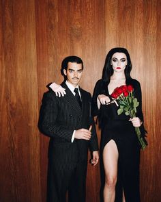 a man and woman dressed in black standing next to each other with roses on their lapels