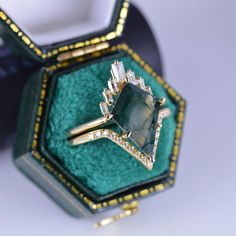 an emerald colored ring with diamond accents in a green velvet box on a white surface