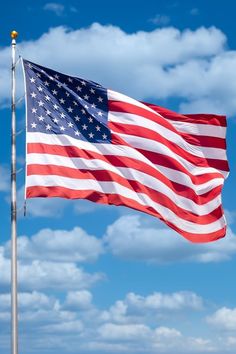 an american flag waving in the wind on a sunny day with blue sky and clouds