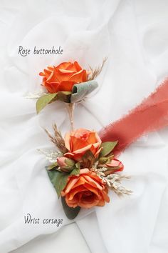 two boutonnieres with orange roses and green leaves on white fabric, labeled rose buttonhole wrist corsage