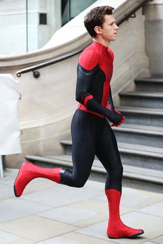 a man dressed as spider - man is running down the street in front of some stairs