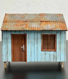 a small blue house with two doors and a rusty tin roof on top of a black table