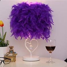 a white table topped with a wine glass and a purple feather ball on top of it