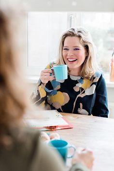 a woman sitting at a table holding a cup