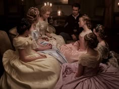 a group of people sitting around each other in dresses and tiaras with candles on the wall behind them