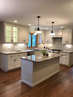 a large kitchen with white cabinets and an island in the middle of the room is lit by two pendant lights