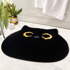 a black cat rug with yellow eyes on the floor next to a potted plant