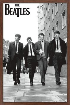 the beatles walking down a city street in black and white, with one man wearing a suit