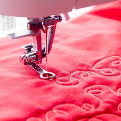 the sewing machine is on top of the red fabric with white stitching and letters